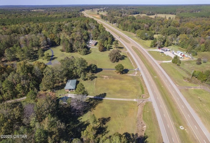 Expansive aerial landscape featuring a residential property with a metal roof and surrounding mature trees