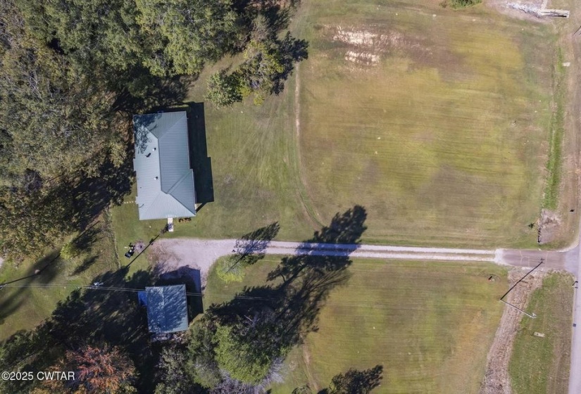 Property featuring a primary residence with a green roof, a secondary structure with a gray roof, extensive green space, mature trees, and a gravel driveway