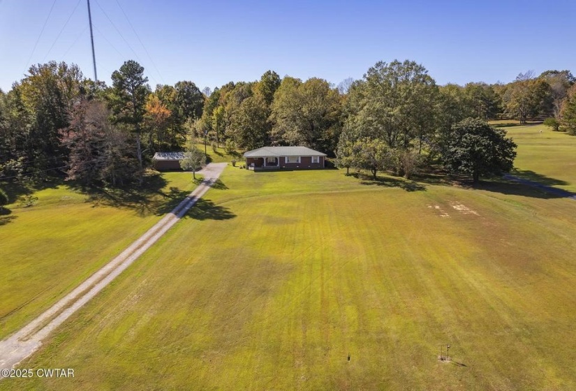 Expansive grassy property featuring a residence with a brick exterior and a dark roof