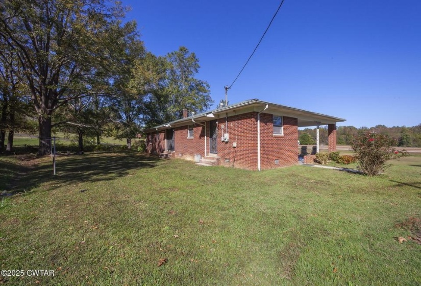Brick exterior with a covered porch, featuring a side entry and a large grassy yard with mature trees