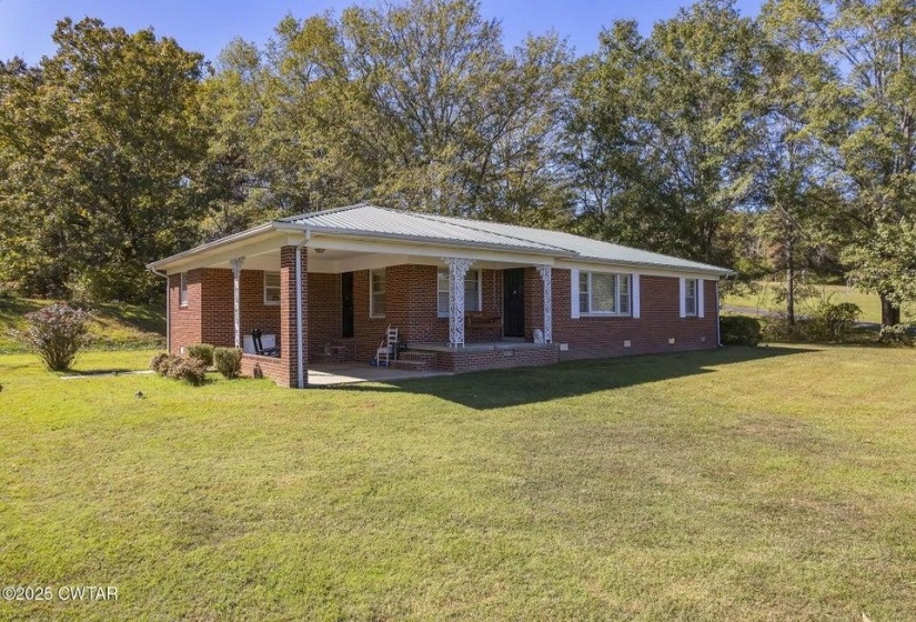 Brick ranch-style exterior featuring a covered front porch with decorative white columns, a metal roof, and a broad front lawn