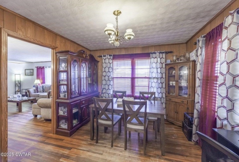 Dining area featuring wood-finish flooring, wood paneling, and an overhead brass chandelier