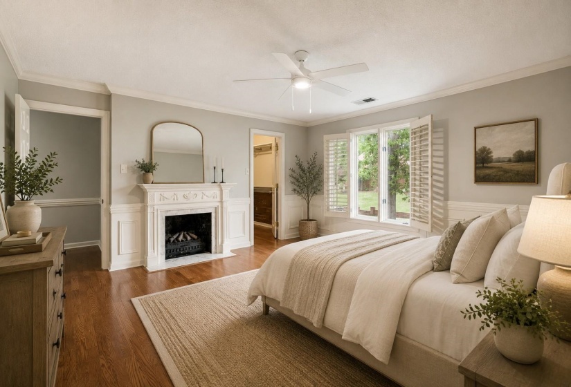 Spacious Bedroom 3 with hardwood flooring, ceiling fan, walk-in closet, second fireplace with electric logs, and beautiful crown, chair, and shadowbox molding. Virtually staged photo.