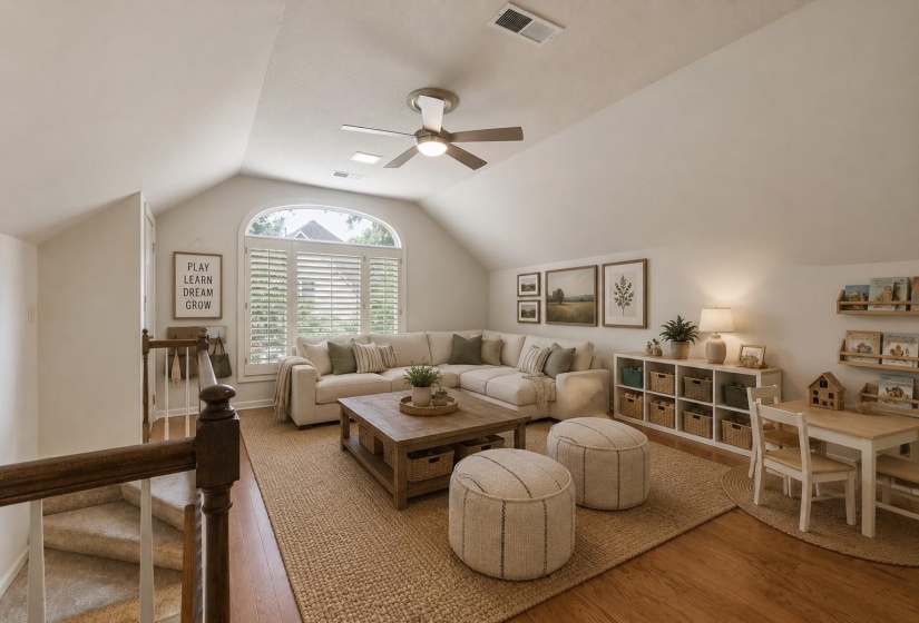 Spacious Playroom accessed by rear stairs, featuring hardwood flooring, ceiling fan, and three closets for exceptional storage. Virtually staged photo.