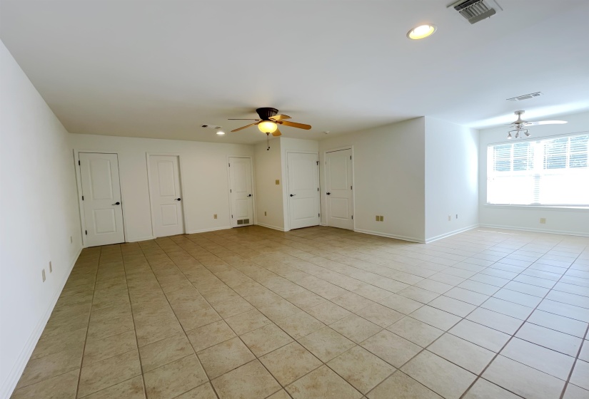 Spacious interior featuring neutral tile flooring, white walls, multiple panel doors with black hardware, and two ceiling fans with integrated lighting