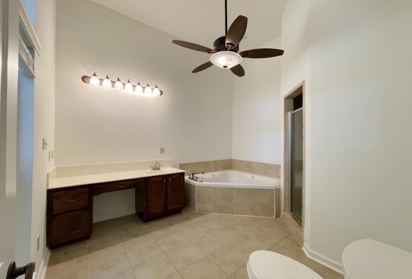 Vaulted ceiling bathroom featuring a corner jetted tub, separate shower enclosure, and a vanity with a single sink and expansive countertop space