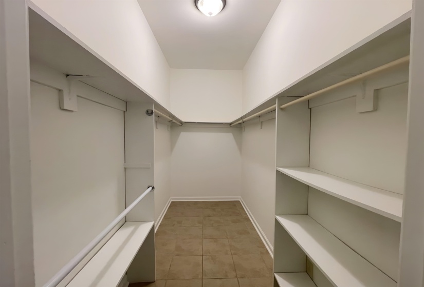 Walk-in closet featuring built-in shelving, multiple hanging rods, white painted walls, white trim, and a tiled floor