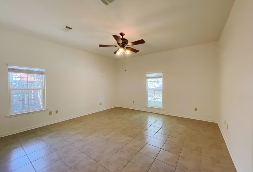 Spacious room featuring vaulted ceilings, two double-hung windows with horizontal blinds, a ceiling fan with light kit, and large square tile flooring
