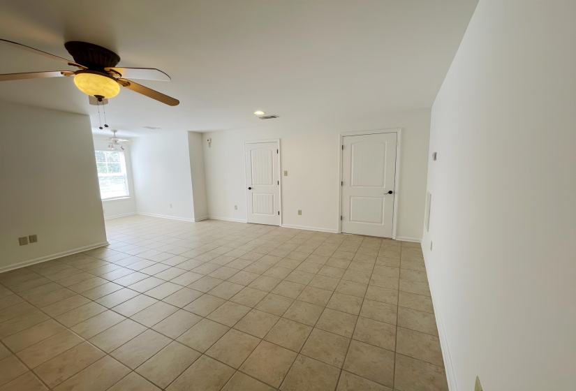 Spacious room featuring neutral-toned tile flooring, white walls, two paneled doors, and an overhead ceiling fan with integrated lighting