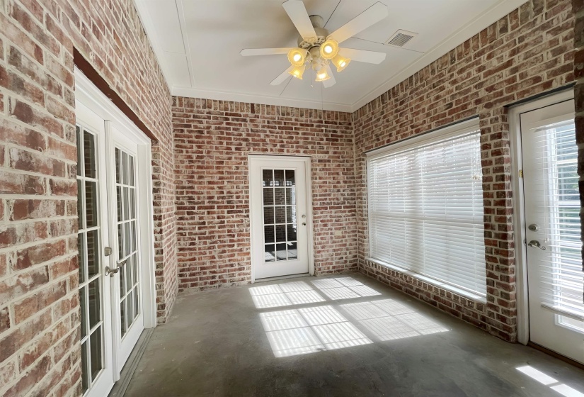 Enclosed sunroom featuring brick walls, concrete flooring, dual French doors, a large window with blinds, and a ceiling fan with integrated lighting