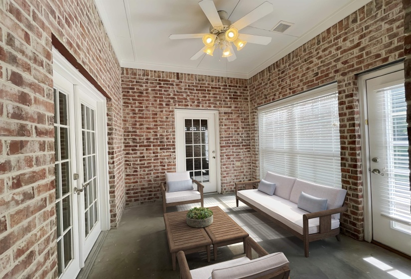Screened porch with exposed brick walls, white ceiling fan, and white trim