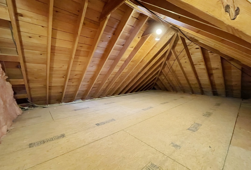 Unfinished attic space featuring exposed wood rafter system, wood plank ceiling, partially insulated wall, and light wood-finish flooring