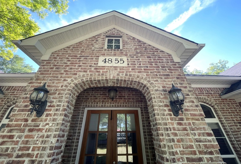 Brick facade featuring an arched entryway, double wood-frame glass panel doors, and two exterior sconces