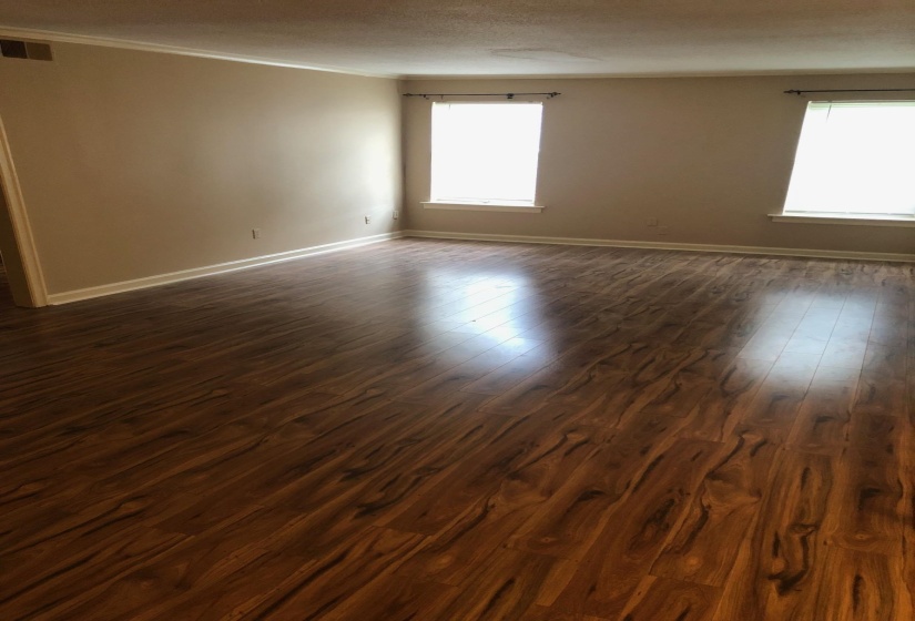 Spacious room featuring wood-finish flooring, neutral-toned walls, white trim, and two windows with blinds
