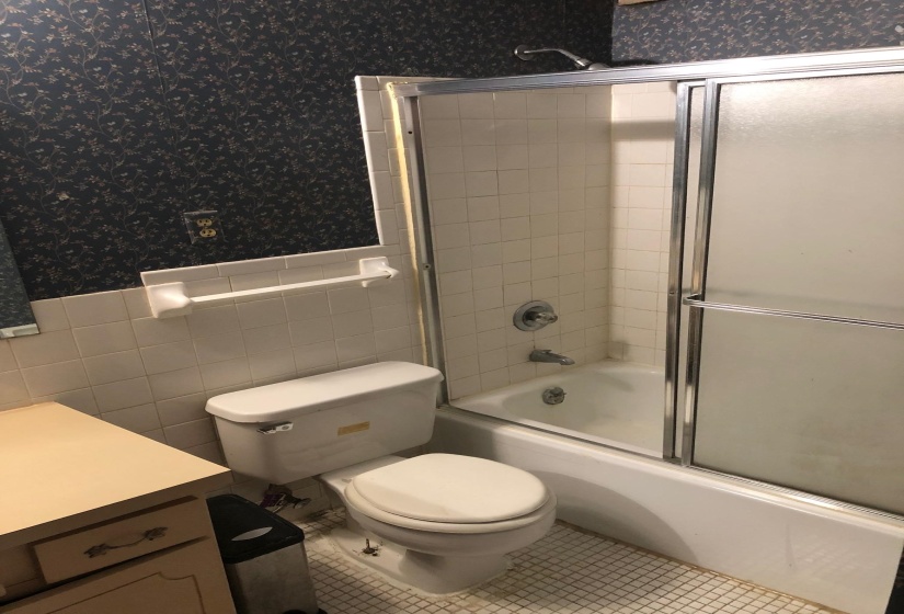 Bathroom featuring a white toilet, tile flooring, and a tub-shower combination with sliding glass doors