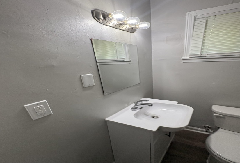 Bathroom featuring a white vanity with integrated sink, chrome faucet, wall-mounted mirror, and an overhead three-bulb light fixture