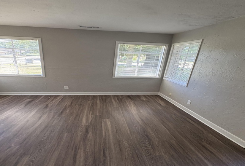 Spacious room featuring wood-finish flooring, light gray walls, and multiple windows with blinds