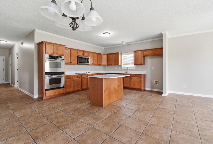 Kitchen featuring wood cabinetry, stainless steel double wall ovens, a central island with countertop, and tile flooring