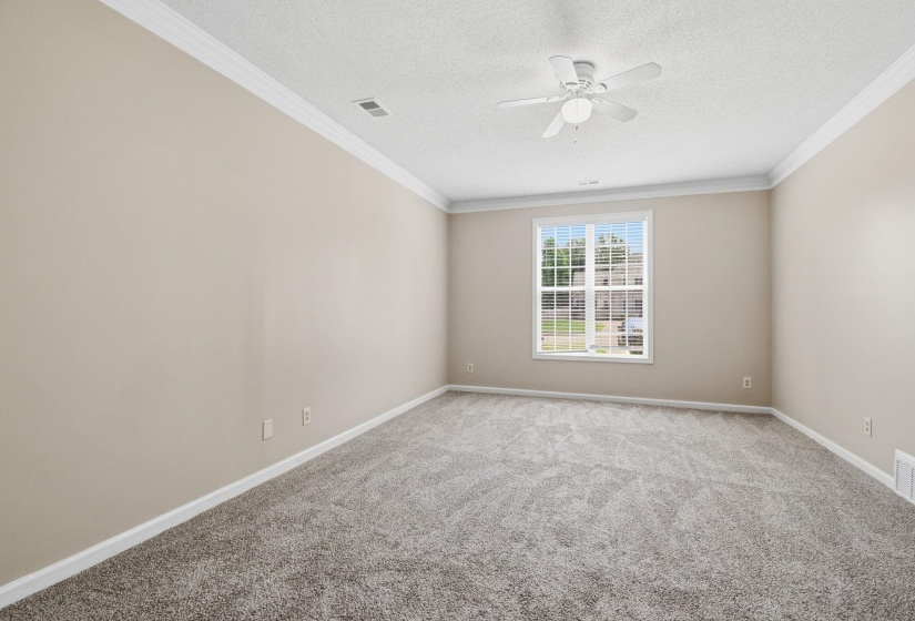 Spacious room featuring neutral paint, gray carpeting, a ceiling fan, crown molding, and natural light from a window with blinds