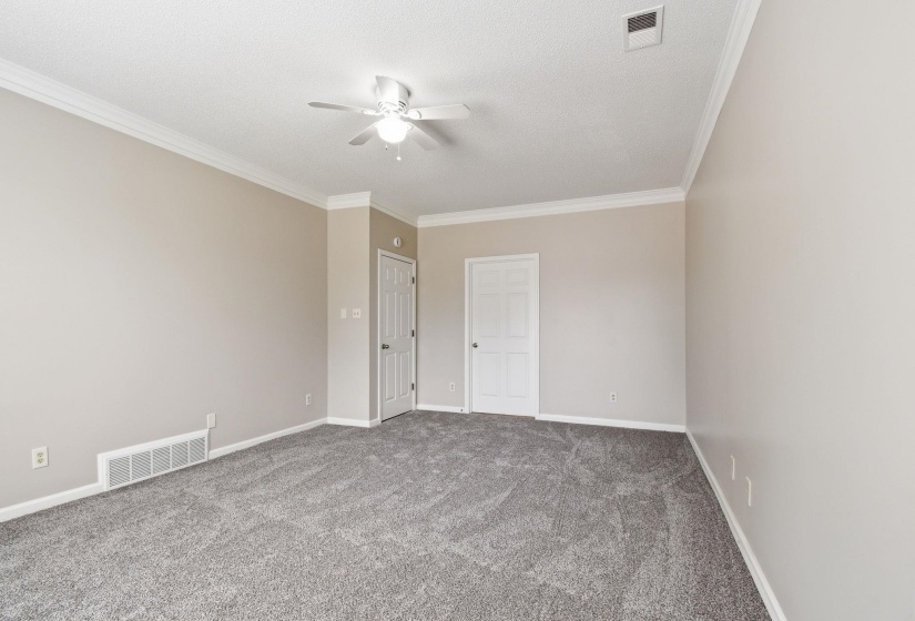 Spacious interior room featuring neutral wall paint, crown molding, a ceiling fan with light fixture, gray patterned carpet, and two paneled interior doors