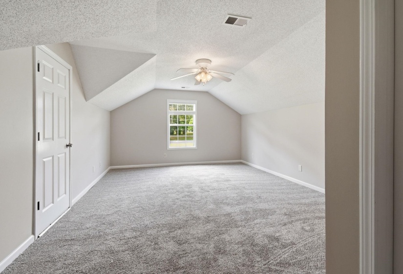 Spacious room featuring vaulted ceilings, a central window, ceiling fan with light fixture, and plush grey carpeting