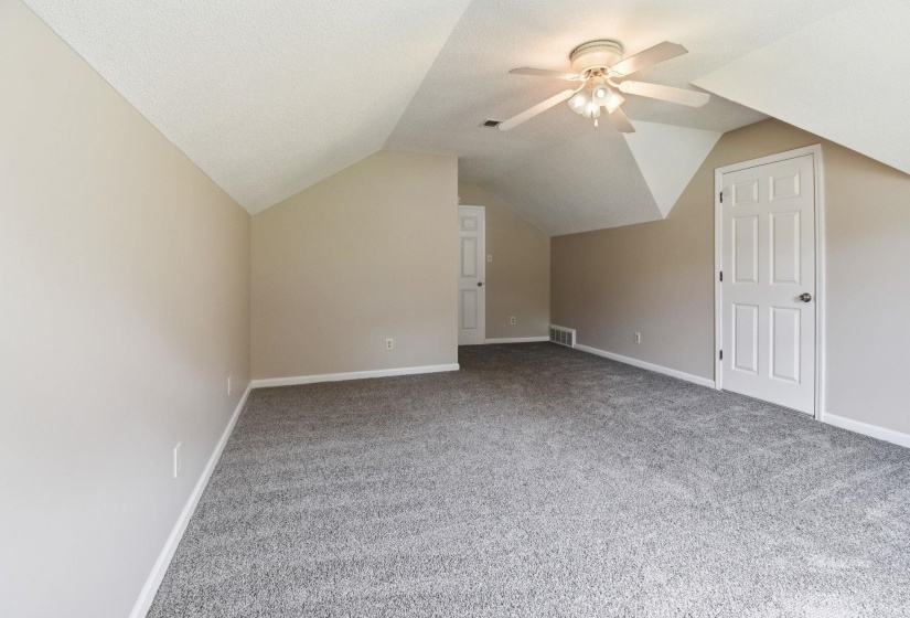 Spacious room featuring vaulted ceilings, a ceiling fan with integrated lighting, neutral wall paint, and gray carpet flooring