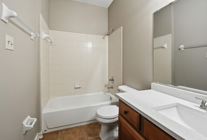 Bathroom featuring a white tub with subway tile surround, a built-in wooden vanity with a white countertop and integrated sink, a toilet, and a wall-mounted mirror
