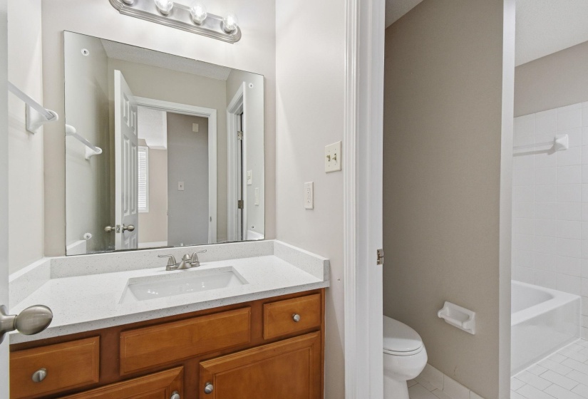Bathroom vanity featuring a light wood-finish cabinet with silver hardware, an integrated white sink, and a speckled white countertop