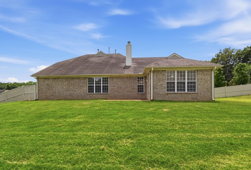 Expansive green lawn bordering the rear of the property, featuring a full brick exterior and multiple windows