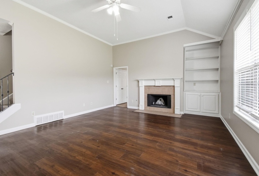 Spacious living area featuring high vaulted ceilings, wood-finish flooring, and a fireplace with a stone surround and a detailed mantel