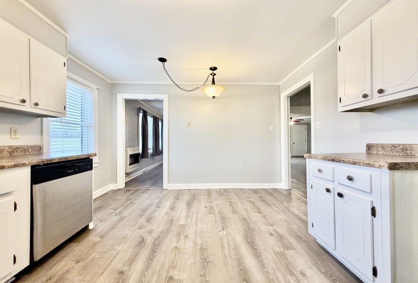 Kitchen with white cabinetry, light wood-style floors, stainless steel dishwasher, ornamental molding, and heating unit