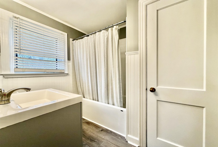 Bathroom with a wainscoted wall, vanity, dark wood finished floors, shower / tub combo, and ornamental molding