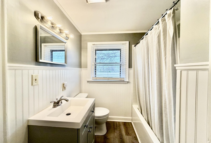 Bathroom featuring wainscoting, vanity, dark wood-style floors, shower / tub combo with curtain, and crown molding