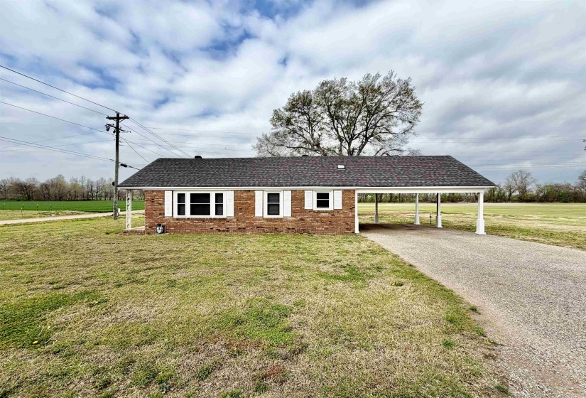 Single story home featuring a front yard, a carport, brick siding, driveway, and a shingled roof