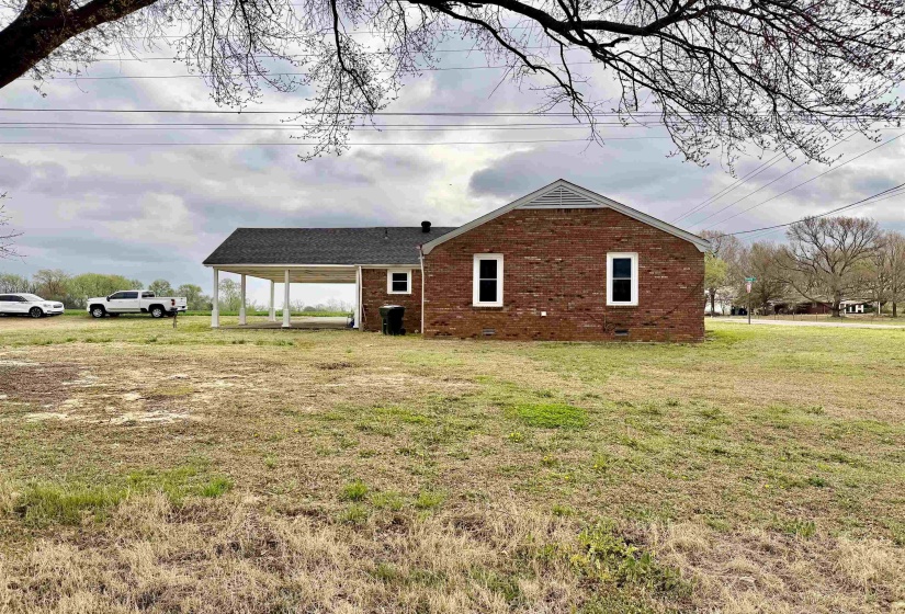 View of side of property featuring brick siding, a yard, and an attached carport