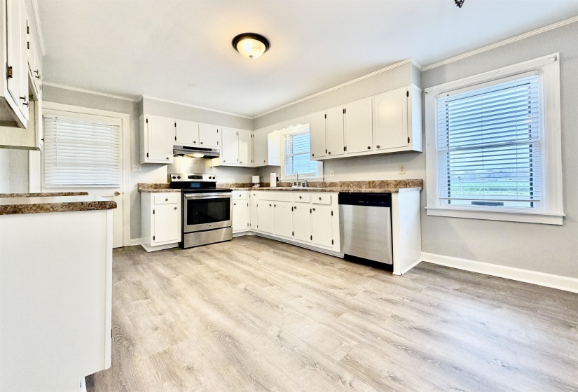 Kitchen featuring stainless steel appliances, white cabinetry, light wood finished floors, ornamental molding, and dark countertops