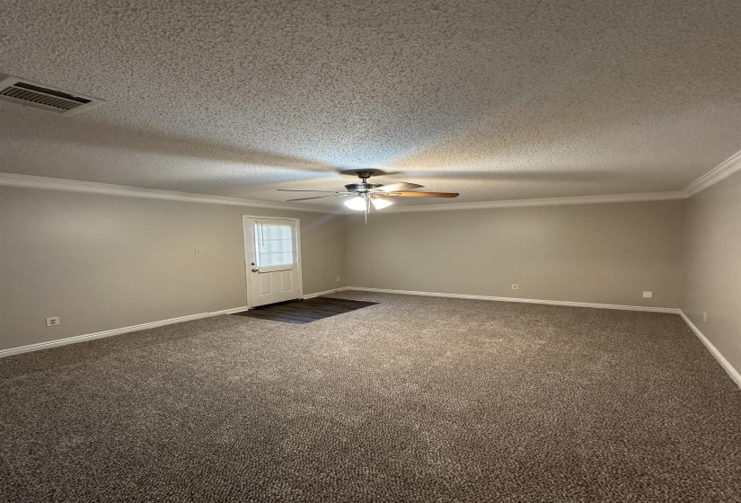 Spacious room featuring new carpeting, crown molding, a ceiling fan, and a rear exterior door with glass inserts
