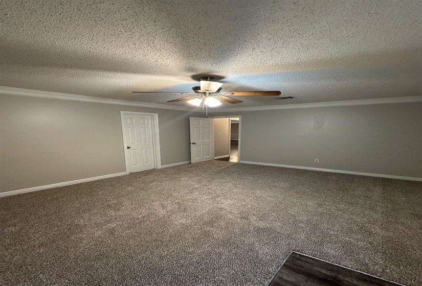 Spacious room featuring new carpeting, neutral wall colors, white trim, a ceiling fan with light fixture, and two panel doors