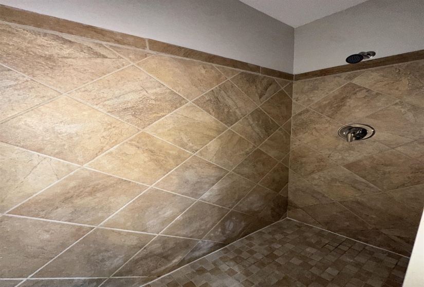 Shower stall featuring diagonal-set wall tiles, mosaic floor tiles, a chrome shower head, and a matching chrome control handle