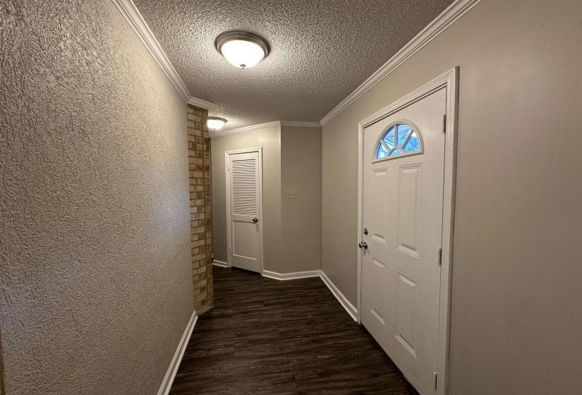 Entryway featuring wood-finish flooring, a white paneled door with an arched glass insert, crown molding, and a brick-finish accent wall