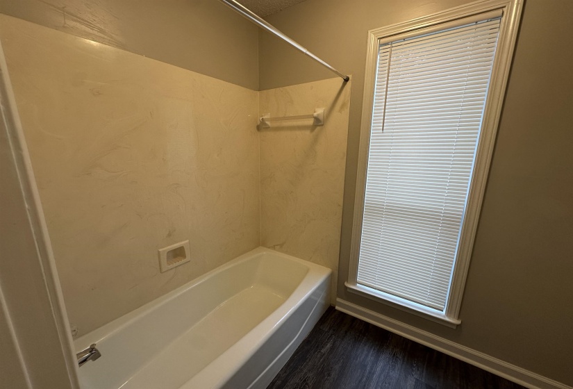 White bathtub with integrated soap dish, surrounded by a light-toned shower surround