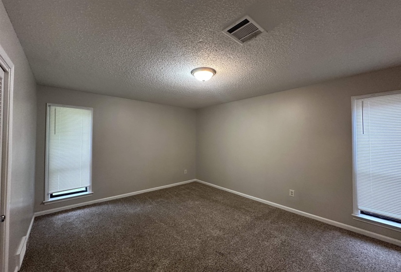 Carpeted room featuring neutral-toned walls, two windows with blinds, a flush mount ceiling light, and white baseboards