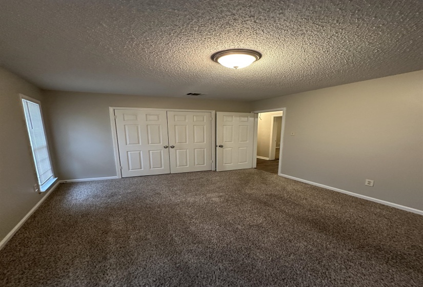 Carpeted room featuring a ceiling-mounted light fixture, two-panel bifold closet doors, a single window with blinds, and neutral wall paint