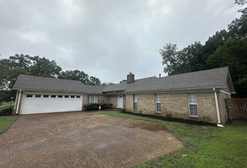 Brick exterior home featuring a multi-car garage, mature landscaping, and a broad driveway