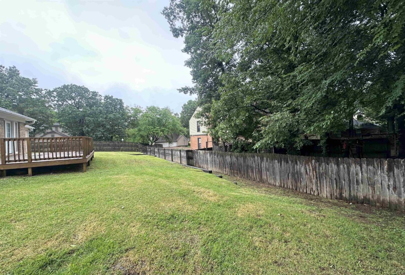 Expansive lawn area featuring a wooden privacy fence, mature trees, and a raised wooden deck
