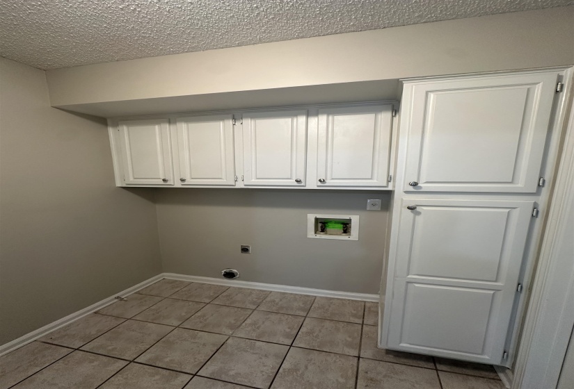 Dedicated utility space featuring extensive white cabinetry, a tall storage pantry, and tile flooring