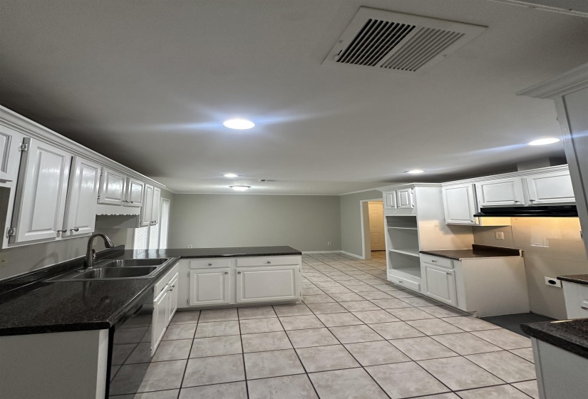 Kitchen featuring white cabinetry, dark countertops, a double basin sink with a gooseneck faucet, tile flooring, and recessed lighting