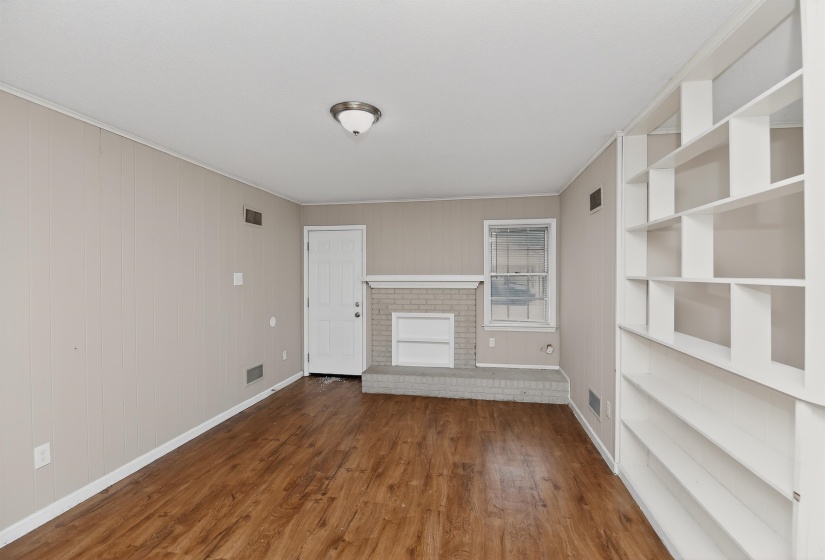 Living area featuring wood-finish flooring, a brick fireplace with a white mantel, and built-in shelving