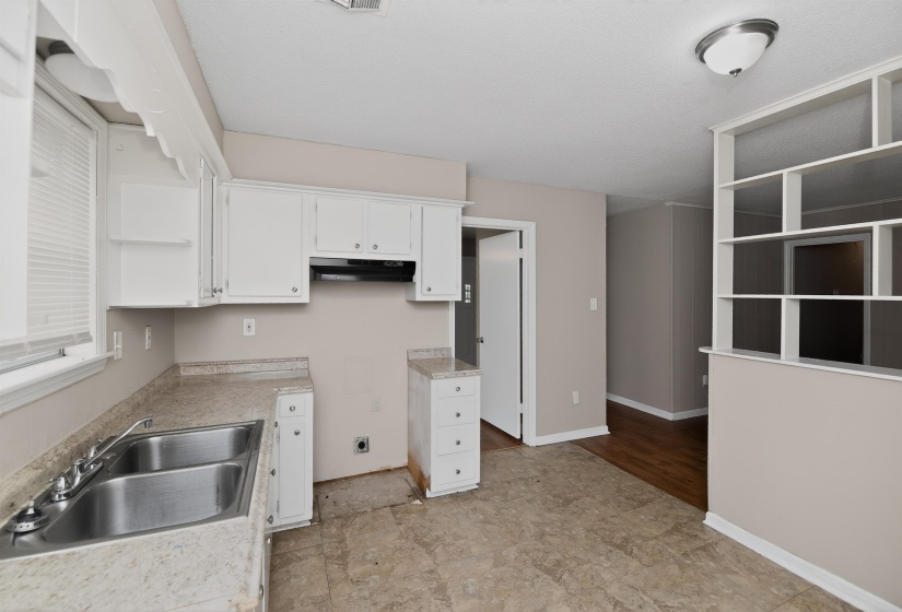 Kitchen area featuring white cabinetry, a double-basin stainless steel sink, and light-toned countertops