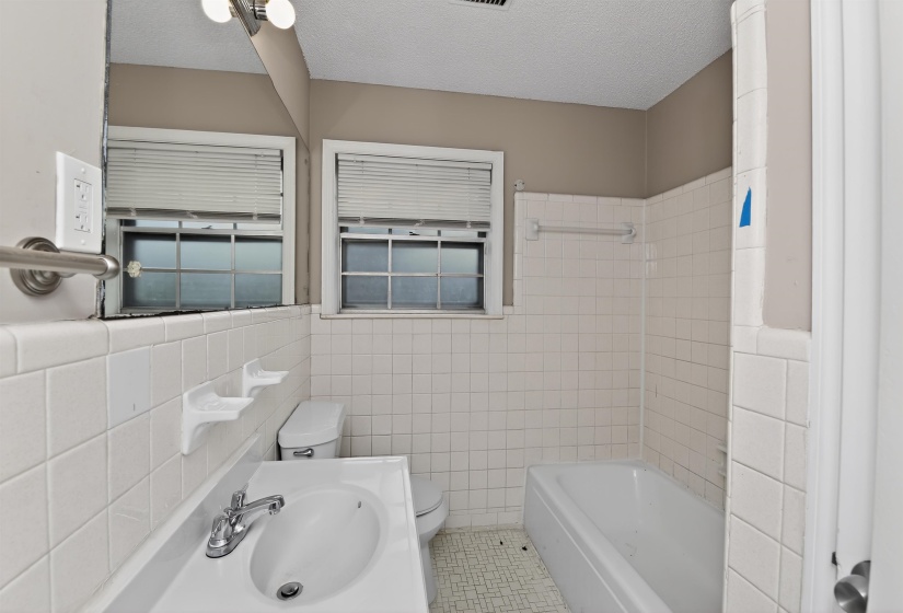 Bathroom featuring white tiled walls, a white vanity with an integrated sink, and a white bathtub with a shower surround